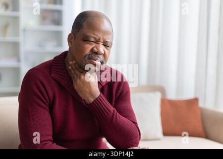 Mature black man touching throat, experiencing sore throat at home Stock Photo