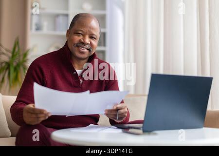 Mature black man holding documents and smiling while reviewing papers at home Stock Photo