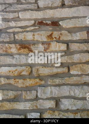 Natural stone wall with irregularly shaped stones in beige, gray, and brown shades. Gray mortar highlights the structure. Rough and rustic. Close-up. Stock Photo