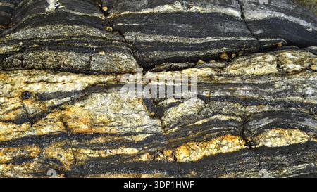Rock of varying compositions, stratified in layers of light and dark colours on the shores of the ocean. Stock Photo