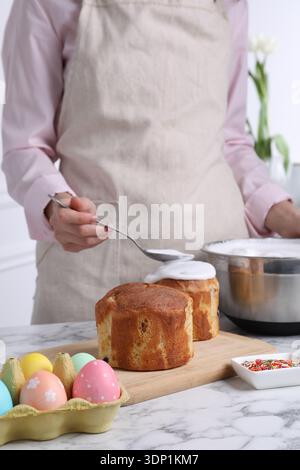 Woman decorating traditional Easter cake with glaze at white marble table indoors, closeup Stock Photo