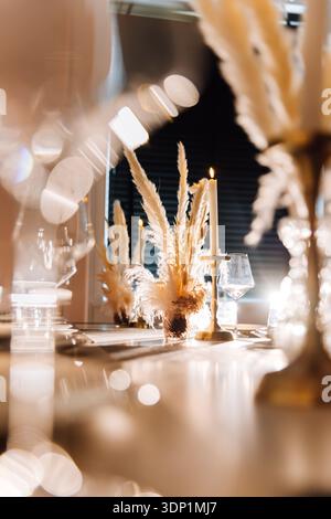 Sunlit restaurant table with candle and pampas centerpiece, elegant decor Stock Photo