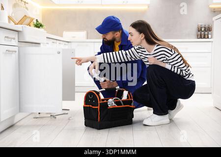 Young woman pointing at pipes to plumber in kitchen Stock Photo