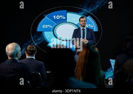 Male business expert hosting presentation and giving inspirational speech, highlighting networking for development. Public speaker on stage engages audience at event in conference hall. Stock Photo