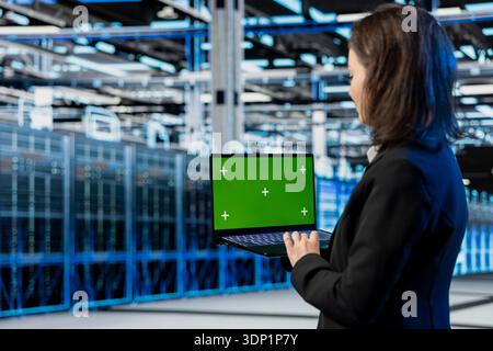 Green screen laptop used by server farm admin to do maintenance on equipment, AR visualization graphics. IT specialist monitoring data center supercomputers with mockup notebook device, VFX holograms Stock Photo
