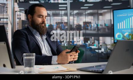 Scrolling smartphone apps as addictive habit and office work distraction, doomscrolling on social media and browsing through emails or texts. Adult CEO checking mobile phone applications. Stock Photo