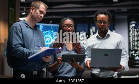 Portrait of engineering team developing artificial intelligence algorithms in high rise office. Teamworking colleagues debug 3D neural network brain models shown on screen Stock Photo