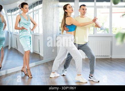 Couple practicing passionate tango guided by female dance instructor in studio Stock Photo