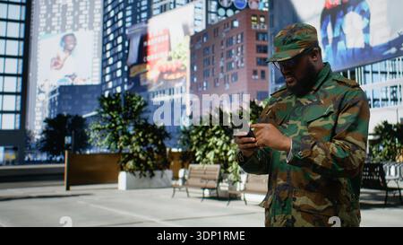Adult male soldier in uniform navigates mobile screen on downtown street, showing disciplined confidence and respectful presence as he checks online page near urban buildings. Camera B. Stock Photo