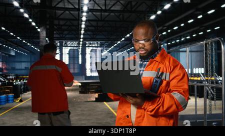 Industrial worker standing near steel machinery during construction tasks, showcasing production responsibility within the factory plant. Power in manufacturing process. Stock Photo