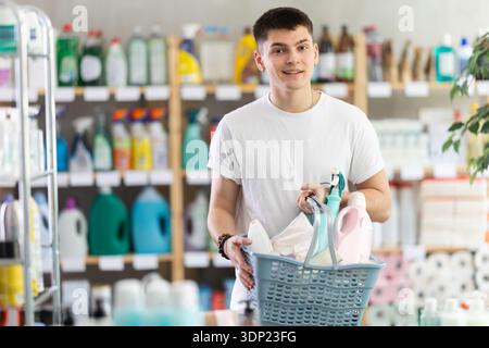 Guy selects various household cleaning products for cleaning the house with full basket of various purchases Stock Photo