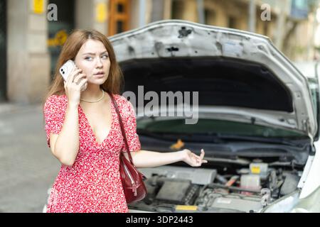 woman stands near a broken car with a phone in her hands Stock Photo