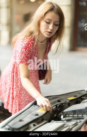 Young woman is worried about her car breaking down on city street Stock Photo
