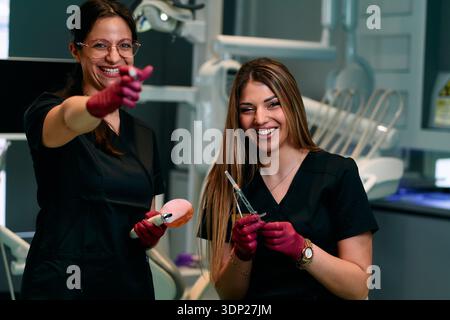 Two Friendly Dental Assistants Share a Laugh While Preparing Tools in Modern Clinic Stock Photo