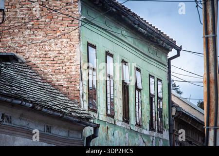 Close view of a decaying facade on an old building in Belgrade, Serbia, with peeling green paint, exposed brickwork, cracked plaster, worn wooden wind Stock Photo