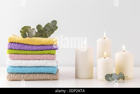 Stack of colorful bath towels, branch of eucalyptus and candles over pastel background Stock Photo