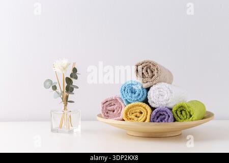 Stack of rolled colorful bath towels on the shelf over light grey background Stock Photo
