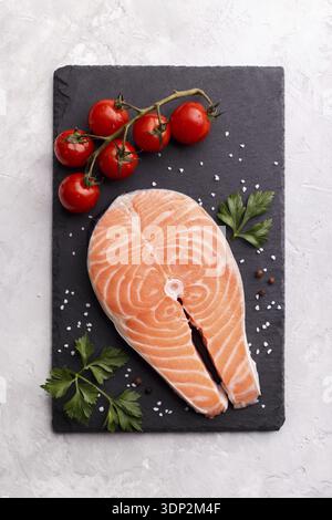 Slice of red fish salmon with herbs and spices on black slate stone board over grey background vertical Stock Photo