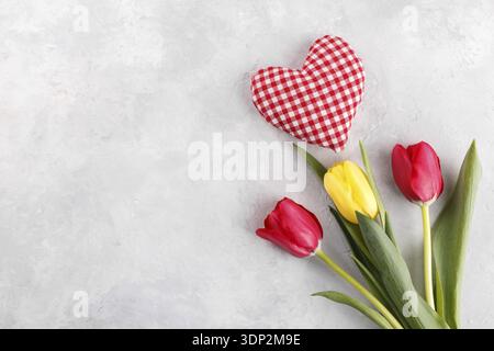 Yellow and red tulips with fabric heart on grey stone background copy space flat lay Stock Photo