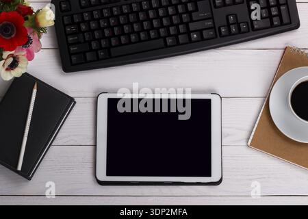 Overhead of office table with computer keyboard, tablet, notepad, coffee mug and book Stock Photo