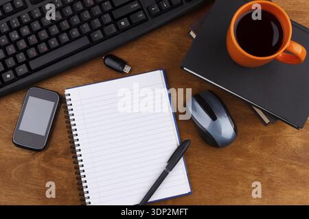 Overhead of office table with computer keyboard, mouse, smartphone, usb, notepad, coffee mug and books Stock Photo