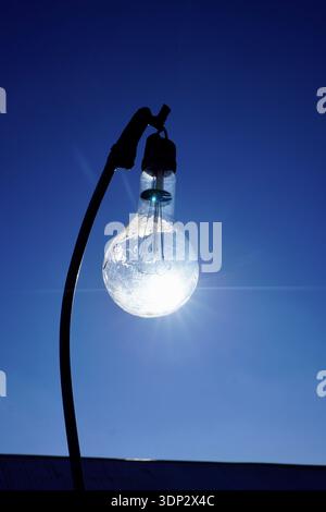 A light bulb on a pole with the background of the blue sky, part of farming equipment. The sun shines through the light bulb. Stock Photo