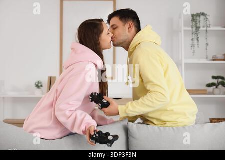 Young couple with game pads kissing at home Stock Photo