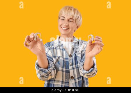 Mature woman with hearing aids on  yellow background Stock Photo