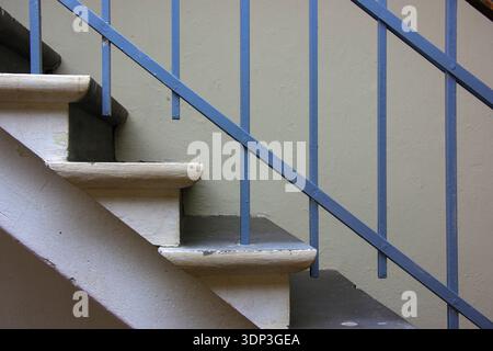 Minimalist interior staircase featuring a blue metal railing with vertical bars. The stairs are constructed of concrete with light beige steps, contra Stock Photo