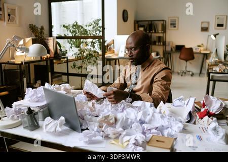 Black Man Analyzing Documents at Desk in Busy Office Environment Stock Photo