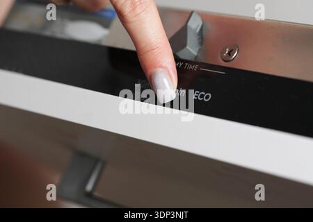 Woman hand detail on modern dishwasher control panel activating cycle. Finger presses program button for eco mode or quick 30 minute wash cycle Stock Photo