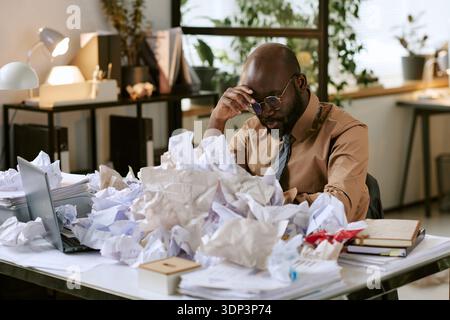 Black Man Sitting at Desk Feeling Stressed in Office Environment Stock Photo