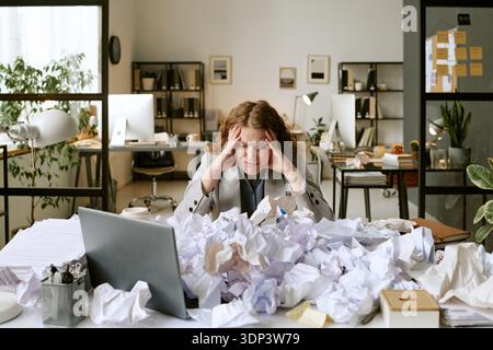 Young Woman Struggling with Paperwork Overload at Office Desk Stock Photo