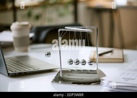 Newton Cradle Swinging on Office Desk Representing Business Momentum Stock Photo