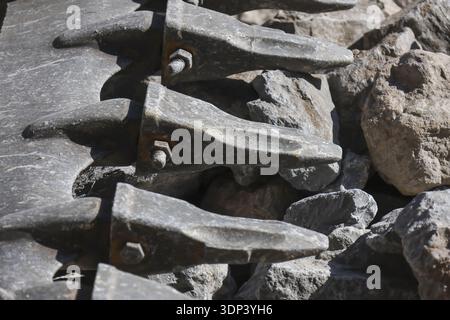 Close up of heavy equipment bucket tooth made of worn metal and steel on pile of rock at construction site. Industrial background showing powerful mac Stock Photo