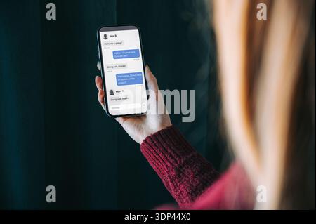 Close-up of a woman holding a smartphone displaying a messaging app conversation. Modern mobile communication concept, ideal for business chat, custom Stock Photo