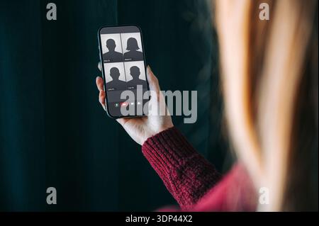 Close-up of a woman holding a smartphone displaying a group video call interface. Modern remote communication concept ideal for online meetings, virtu Stock Photo