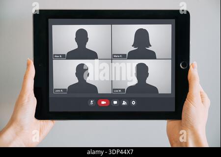 Close-up of hands holding a tablet displaying a video conference interface with silhouette avatars and generic names. Clean, commercial-ready mockup i Stock Photo