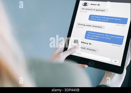 Close-up of a woman holding a tablet displaying a messaging app conversation interface. Modern digital communication concept ideal for online chat, re Stock Photo