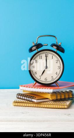 Clock sits on notebooks against a blue backdrop during daytime in a study area Stock Photo