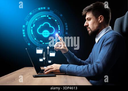 Man works on laptop with cloud data icons in dark room at night Stock Photo