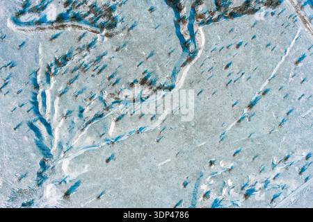 Frozen winter landscape reveals intricate patterns of snow and ice as long blue shadows stretch across the field. A cold, desolate nature scene captured from a high bird's-eye perspective. Stock Photo