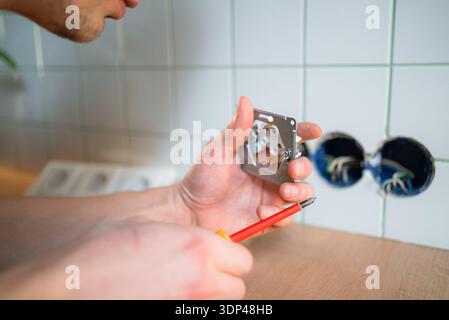 Electrician tightening a kitchen wall socket with a screwdriver, close-up on hands and wiring during home renovation and repair, ensuring safe electrical connection and fit Stock Photo