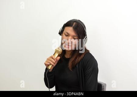 Young woman wearing headphones and glasses singing into microphone isolated on white background music performance and recording concept Stock Photo