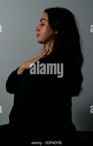 Serene Profile Portrait of a Woman in Black, Reflective Pose with Hand at Neck Stock Photo