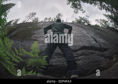 A man stands in front of a natural high granite wall. Back view. Human and obstacle Stock Photo