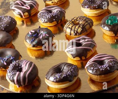 Mini donuts covered in dark chocolate on a gold background. Stock Photo