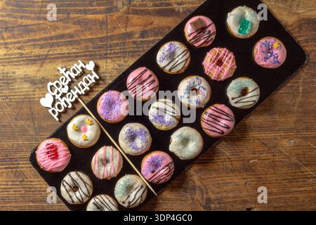 Mini donuts with chocolate and decorations. Next to it is the text in Serbian "Срећан рођендан" (Happy birthday in Serbian). Stock Photo