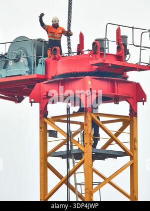 Construction Worker On Tower Crane Wearing Safety Gear At Height On Industrial Site Stock Photo
