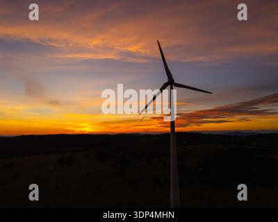Aerial view shows a wind turbine during sunset, highlighting renewable energy in a natural landscape with warm light and dramatic clouds. Stock Photo